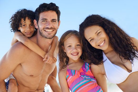 Family getaway. A family of four in swimwear smiling against a bright sky