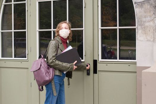 female student in a protective mask holds notes and opens the door to the collegeHigh quality photo