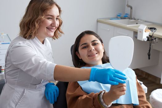 Young Woman Looking At Mirror With Smile In Dentist Office