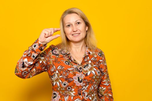 Displeased skeptical woman in print dress gesturing small, undersized, dissatisfied with low rating. Isolated on yellow background