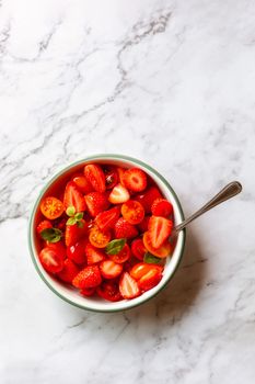 bowl of strawberry, tomato cherry and basil leaves salad, top view, copy space