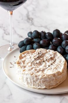 camembert cheese served with grapes and red wine, decorated with thyme branches, side view