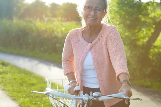 Summer biking. A lovely senior woman standing with her bike beneath a summer sun