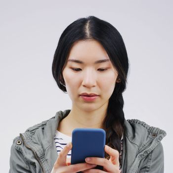 Communication just gets smarter and smarter. Studio shot of a young woman using a mobile phone against a grey background