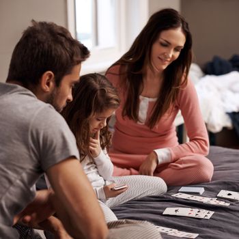 Shes really getting into the game. a young family playing cards together at home