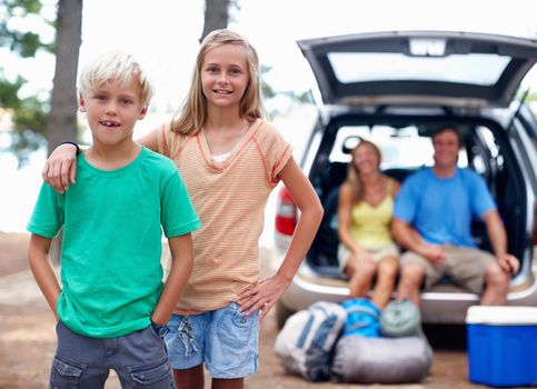 Family enjoying vacation. Portrait of young brother and sister enjoying their vacation with parents sitting in the back of a car