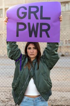 Confident young hispanic woman looking at camera holding a purple Girl power sign above her head in feminist demonstration. Vertical image. Women empowerment concept.