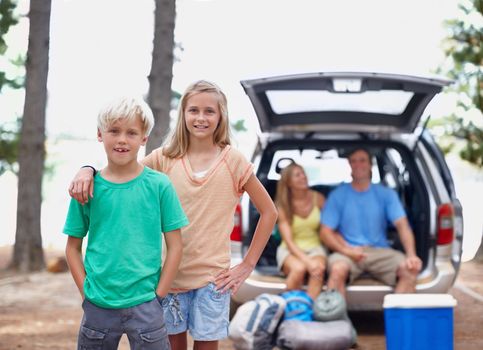 Young siblings enjoying holiday. Portrait of young siblings standing outdoors with parents sitting in a car