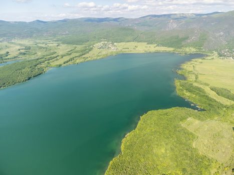 Aerial landscape from flying drone storage reservoir at mountain foot covered colorful spring forest. Beautiful view from above blue lake among highlands