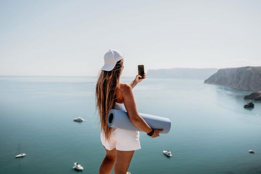 Young woman with black hair, fitness instructor in pink sports leggings and tops, doing pilates on yoga mat with magic pilates ring by the sea on the beach. Female fitness daily yoga concept