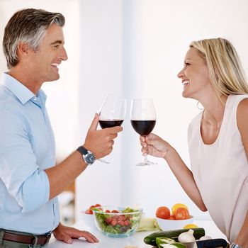 Cheers, babe. an affectionate mature couple toasting with red wine while making dinner