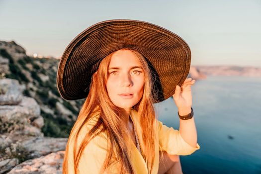 Portrait of happy young woman wearing summer black hat with large brim at beach on sunset. Closeup face of attractive girl with black straw hat. Happy young woman smiling and looking at camera at sea