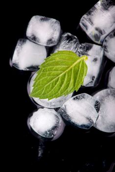 Ice cube with mint leaves on black background