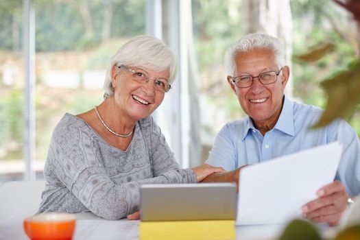 Technology has all the answers. a senior couple using a digital tablet and holding paperwork