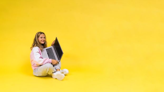 Beautiful little girl sitting on light floor with a gray laptop and smiling, empty space