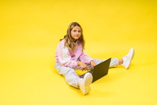 Beautiful little girl sitting on light floor with a gray laptop and smiling, empty space