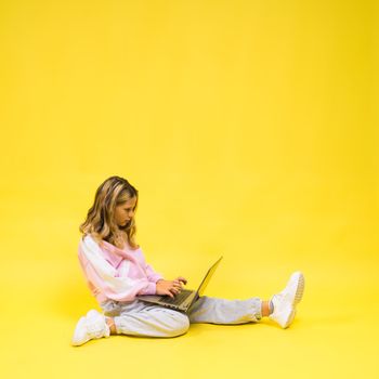 Beautiful little girl sitting on light floor with a gray laptop and smiling, empty space