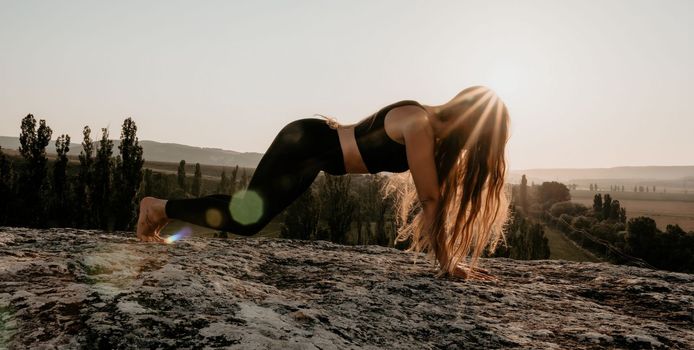Well looking middle aged woman with long hair, fitness instructor in leggings and tops doing stretching and pilates on the rock near forest. Female fitness yoga routine concept. Healthy lifestyle.