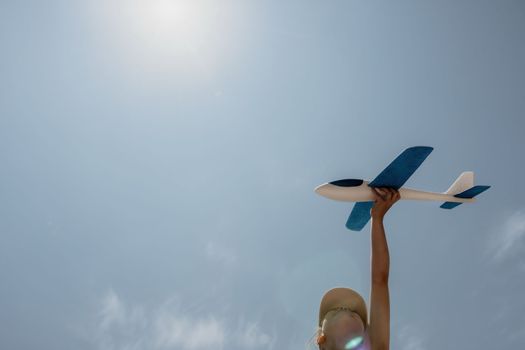 Kid playing with toy airplane. Children dream of travel by plane. Happy child girl has fun in summer vacation by sea and mountains. Outdoors activities at background of blue sky. Lifestyle moment