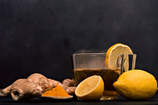 Cup of hot tea with ginger root, lemon and curcuma. Adding natural raw honey to cup of hot tea. Vitamin C drink, immune system boost