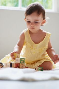 Young learning. a cute baby girl sitting on the floor playing with toy blocks