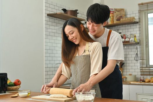 Romantic young couple wearing aprons preparing homemade pastry, enjoying leisure time together at home.