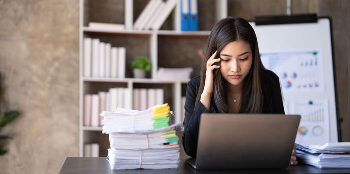 Young Asian businesswoman working on laptop computer, stressed has a headache and thinks hard from work at the office...