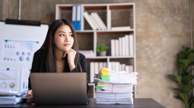 Young Asian businesswoman working on laptop computer, stressed has a headache and thinks hard from work at the office...