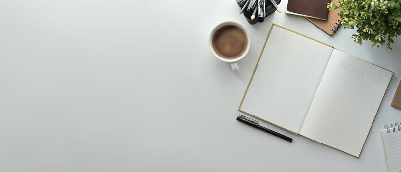 Top view of blank notebook, cup of coffee, pencil holder and houseplant on white table. Copy space for your text.