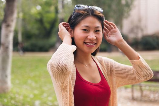 young asian woman looking at camera smiling while putting sunglasses on her hair, concept of youth and beauty
