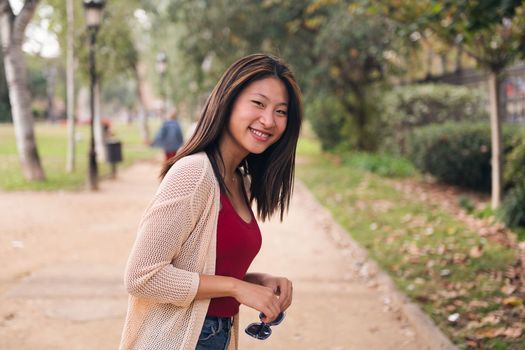 young asian woman smiling happy looking at camera with sunglasses in her hands, concept of youth and beauty