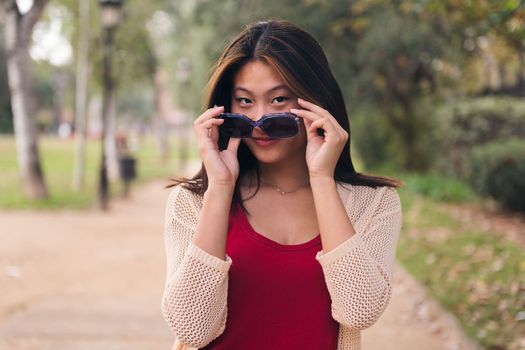young asian woman looking at camera with mischief over her sunglasses, concept of youth and beauty