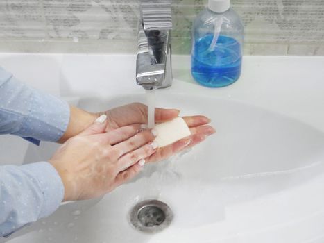 hand washing with soap or gel under running water in the washbasin, cleanliness and hygiene, men's hands dressed in white shirt