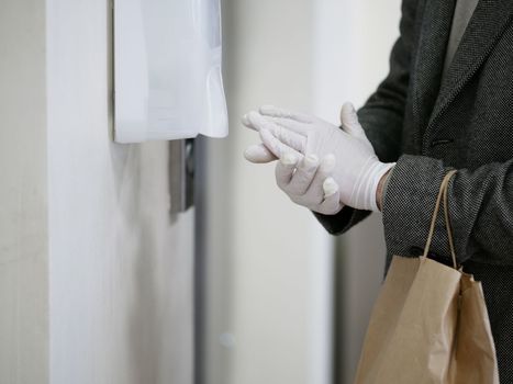 man hands in gloves Using Automatic Alcohol Dispenser to Clean Bacteria and Corona Virus. Dezinfection shopping in moll