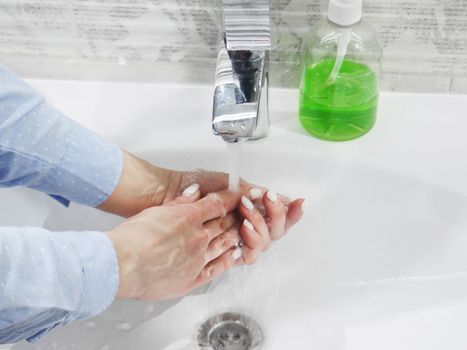 hand washing with soap or gel under running water in the washbasin, cleanliness and hygiene, men's hands dressed in white shirt