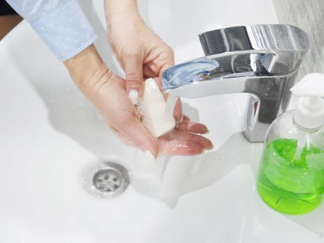 hand washing with soap or gel under running water in the washbasin, cleanliness and hygiene, men's hands dressed in white shirt