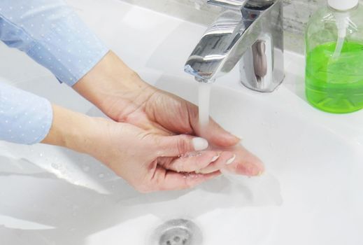 hand washing with soap or gel under running water in the washbasin, cleanliness and hygiene, men's hands dressed in white shirt