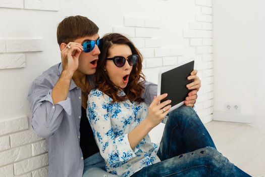 Happy couple with tablet, shopping online, making internet order sitting at home floor in empty living room