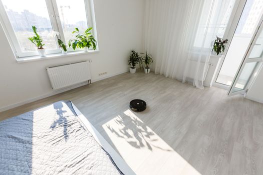 White robotic vacuum cleaner on laminate floor cleaning dust in empty room. Smart electronic housekeeping technology