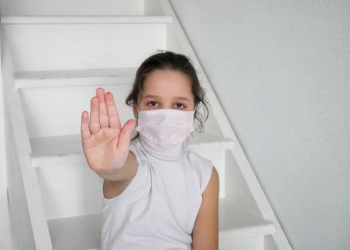 Little girl child in protective face mask showing hand stop sign on white background. Focus at his hand.