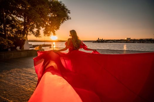 Sunrise red dress. A woman in a long red dress against the backdrop of sunrise, bright golden light of the sun's rays. The concept of femininity, harmony