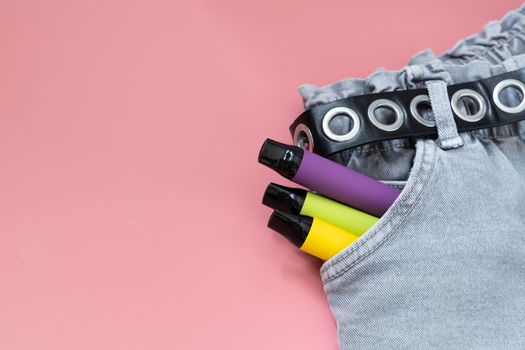 Colorful disposable vapor stick in pocket of jeans on a light background. Concept of modern e-smoking, vaping and nicotine, electronic cigarettes