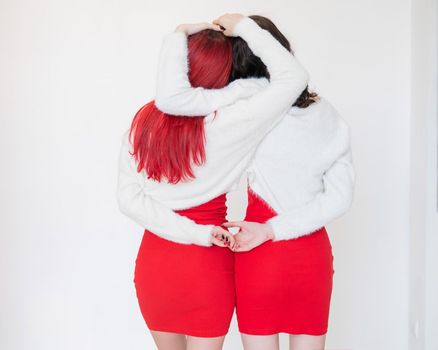 Rear view of two women dressed in identical red dresses and white sweaters. Lesbian intimacy. White background