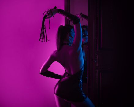 Sexy lover girl in latex bdsm costume and leather cat mask in neon light in front of the mirror copy paste background