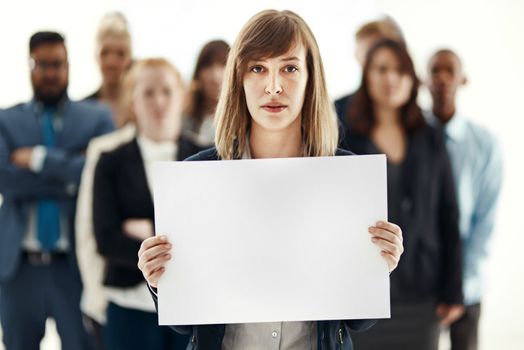 Supported by her team. Portrait of a young businesswoman holding a blank placard with her colleagues in the background