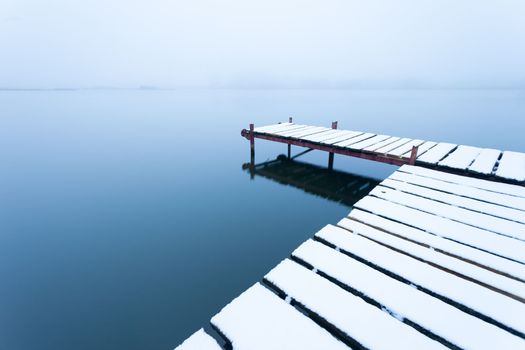 A snow-covered pier with a calm lake on a foggy day, Stankow, Poland