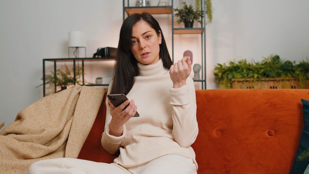 Sad displeased woman use smartphone typing browsing, loses becoming surprised sudden lottery results, bad news, fortune loss, fail, deadline, virus. Young adult brunette girl at home room on couch