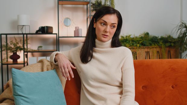 Sad lonely brunette woman sitting at home room looks pensive thinks over life concerns or unrequited love suffers from unfair situation. Girl problem, break up, depressed feeling bad annoyed burnout