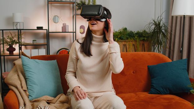Woman using virtual reality futuristic technology VR app headset helmet play simulation 3D 360 video game watching film movie at home apartment. Girl in goggles sitting on sofa. Transition zoom effect