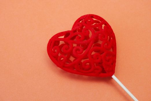 Valentine's Day concept. Copy space. Decorative red gift heart on a stick on an orange background.